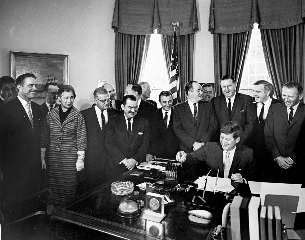 John F. Kennedy signing the Peace Corps Act in 1961 in Oval Office with other people present