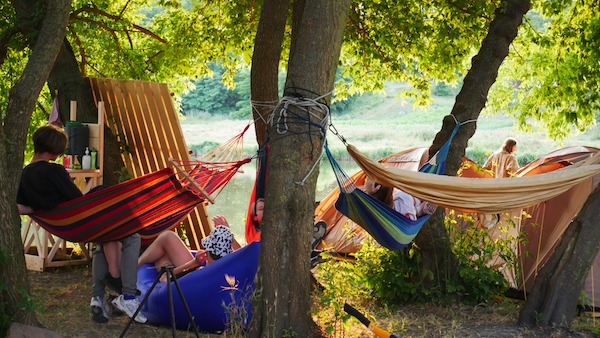 Teens rest in colorful hammocks hanging from trees in late afternoon sunshine