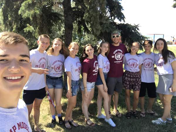 Smiling young people in Model UN t-shirts post together in front of pine trees
