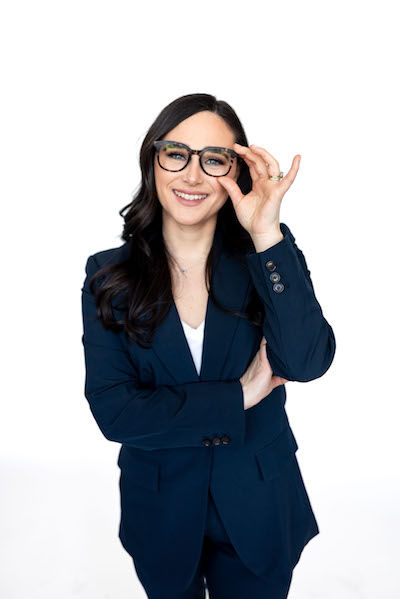 Emily pictured against a white background wearing a navy blue business suit and glasses